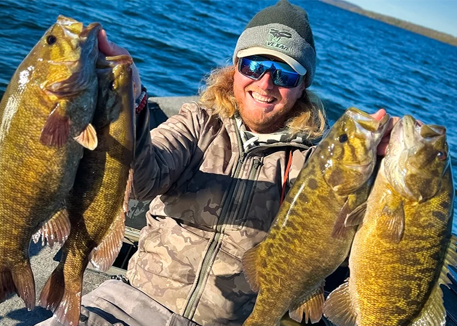Person holding four large bass fish on a boat with a body of water in the background