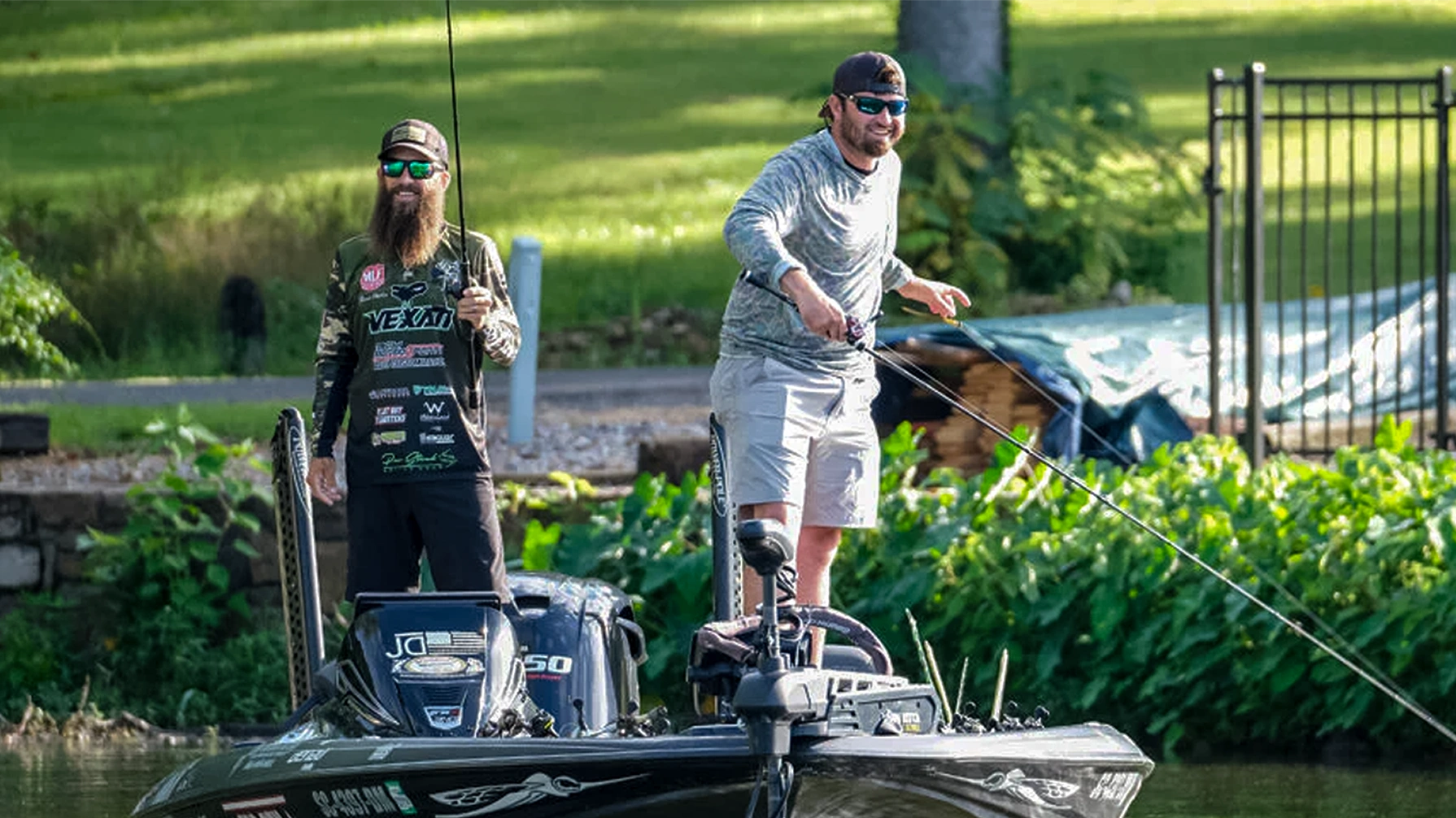 Two men on a boat in a body of water with grass and trees in the background